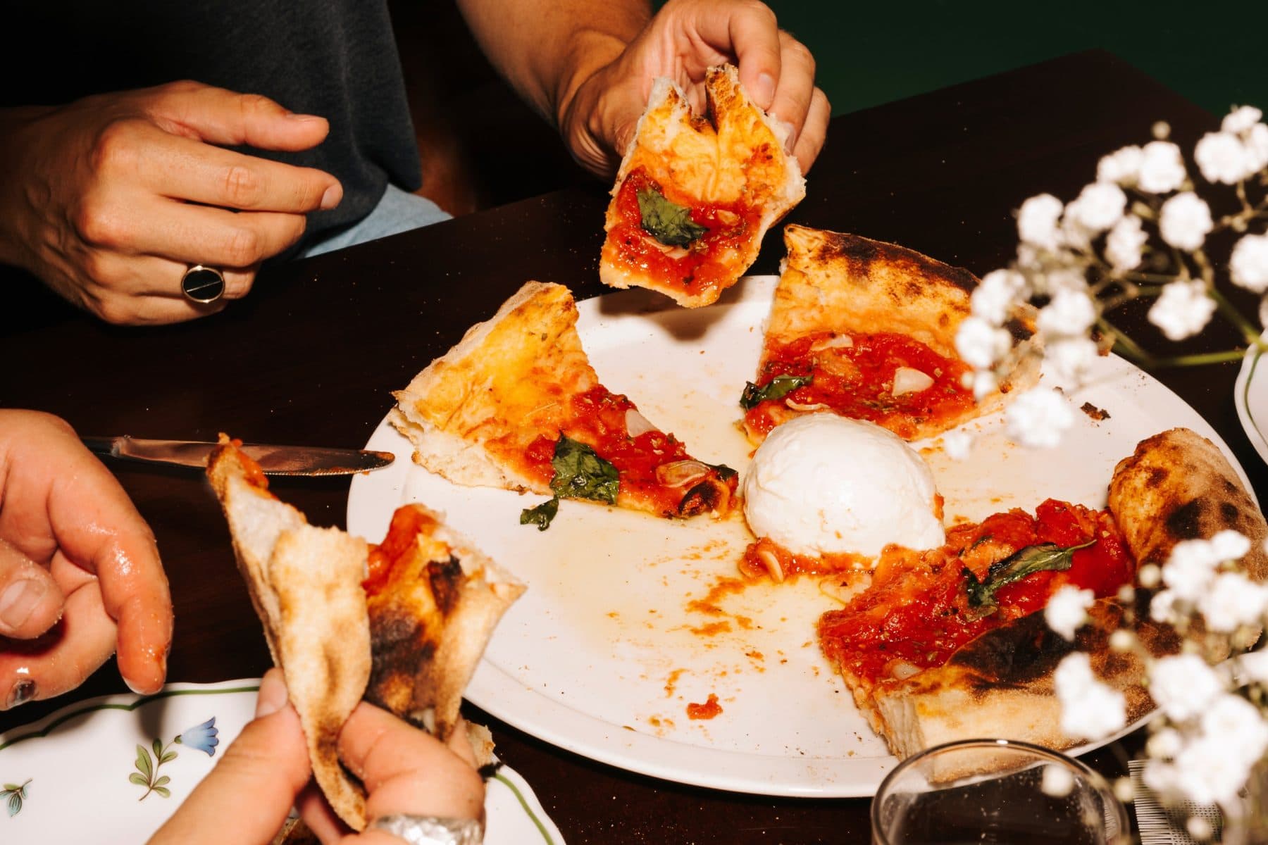 Goście dzielą się świeżą pizzą margheritą na zakwasie przy stole w PIENO